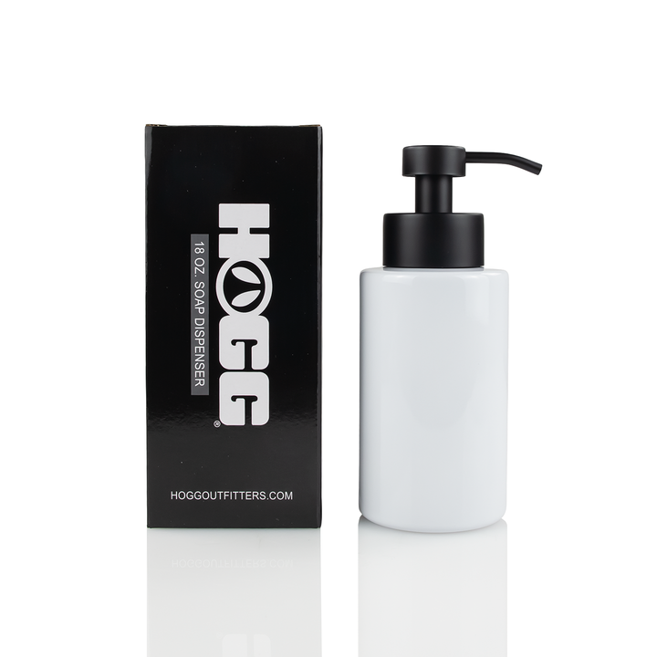 A white soap dispenser with a black pump lid next to its black packaging box with the text 'HOGGOUTFITTERS.COM' on it.